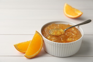 Delicious orange marmalade in bowl with spoon on white wooden table, space for text