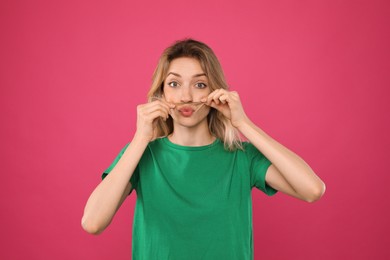 Photo of Funny woman making fake mustache with her hair on pink background