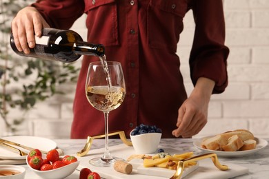 Woman pouring wine from bottle into glass at table with different snacks, closeup