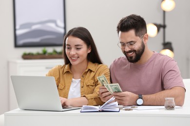 Photo of Happy young couple counting money at white table indoors