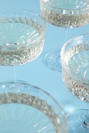 Glasses of expensive white wine on light blue background, closeup