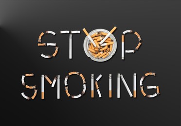 Image of Quitting bad habit concept. Phrase Stop Smoking made of burnt cigarettes and glass ashtray on dark background, flat lay