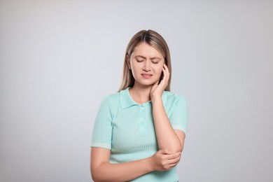 Photo of Young woman suffering from ear pain on light grey background