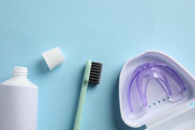 Photo of Bite correction. Toothpaste, brush and dental mouth guard on light blue background, flat lay. Space for text