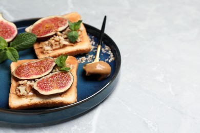 Tasty toasts served with fig, peanut butter and walnuts on white marble table. Space for text