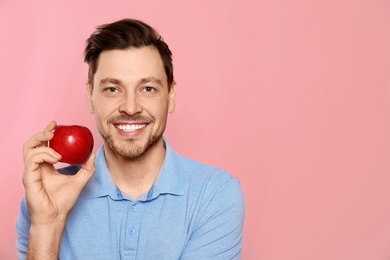 Smiling man with perfect teeth and red apple on color background. Space for text