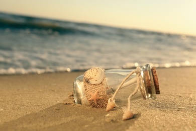 Wedding invitation in glass bottle on sandy beach at sunset