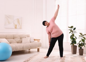 Overweight mature woman stretching at home, space for text