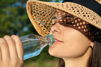 Happy woman in straw hat drinking water outdoors on hot summer day, closeup. Refreshing drink