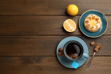 Tea bag in ceramic cup of hot water, dessert and sugar cubes on wooden table, flat lay. Space for text