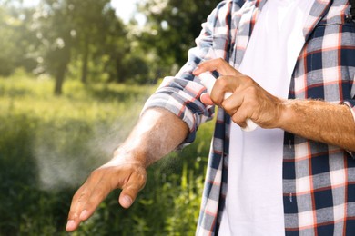 Man spraying tick repellent on arm during hike in nature, closeup