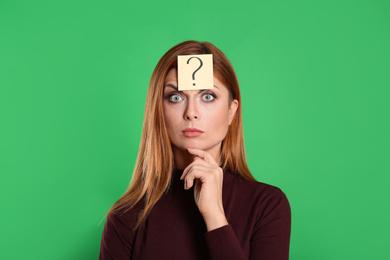Pensive woman with question mark sticker on forehead against green background