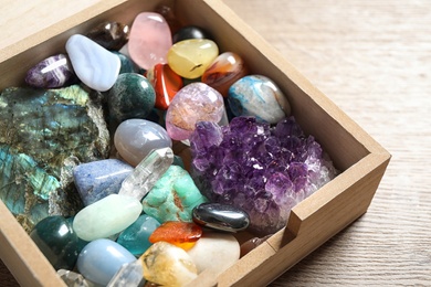 Box with different beautiful gemstones on wooden table