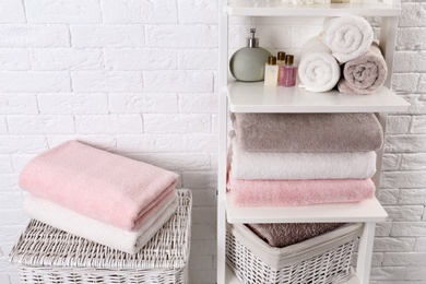 Shelving unit and baskets with clean towels and toiletries near brick wall