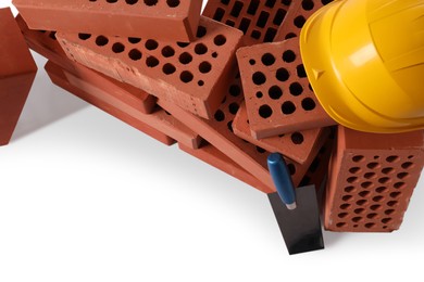 Photo of Many red bricks, hard hat and trowel on white background, above view