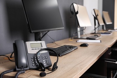 Stationary phone and headset near modern computer on wooden desk in office. Hotline service