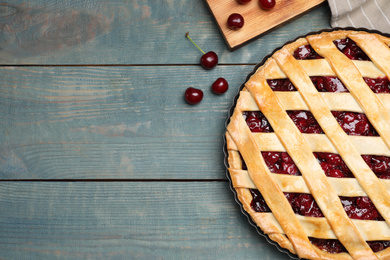 Delicious fresh pie and cherries on light blue wooden table, flat lay. Space for text