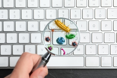 Woman with magnifying glass detecting microbes on keyboard, closeup