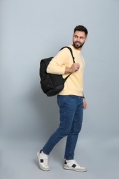 Young man with stylish backpack walking on light grey background