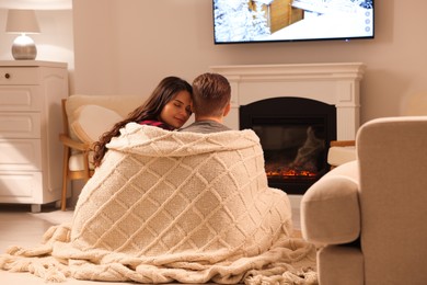 Photo of Lovely couple wrapped in blanket near fireplace at home, back view