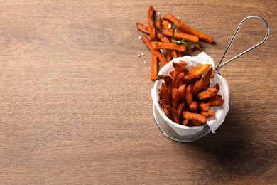 Frying basket with sweet potato fries on wooden table, above view. Space for text