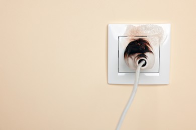 Photo of Burnt plug in power socket on beige wall, space for text. Electrical short circuit