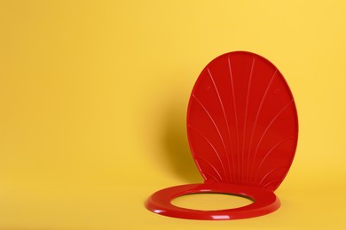 New red plastic toilet seat on yellow background, space for text