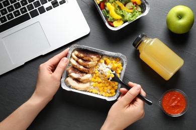 Woman eating from lunchbox at grey table, closeup. Healthy food delivery