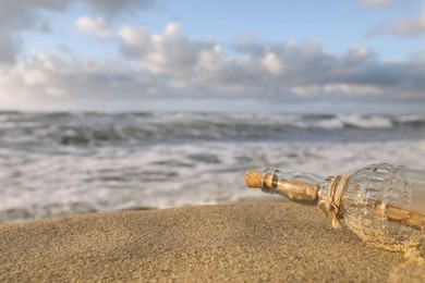 SOS message in glass bottle on sand near sea, closeup. Space for text