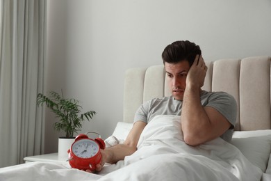 Emotional man with alarm clock in bed. Being late because of oversleeping