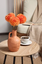 Ceramic vase with beautiful flowers on coffee table near armchair indoors