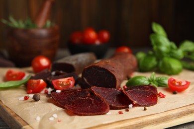 Delicious dry-cured beef basturma with basil, tomatoes and spices on wooden table, closeup