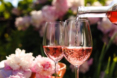 Pouring rose wine into glass in garden, closeup