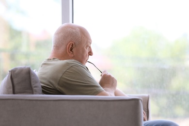 Depressed senior man sitting in armchair indoors
