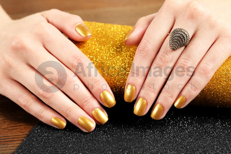Woman showing manicured hands with golden nail polish on table, closeup