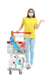 Young woman in medical mask and shopping cart with purchases on white background. Coronavirus pandemic 
