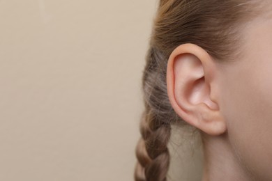 Cute little girl on beige background, closeup of ear. Space for text
