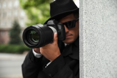 Private detective with modern camera spying outdoors, focus on lens