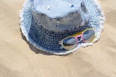 Jeans hat and sunglasses on sand, above view. Beach accessories