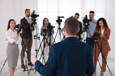 Business man talking to group of journalists indoors, back view