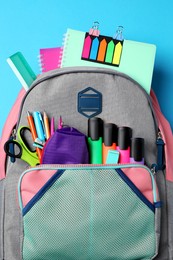 Backpack with school stationery on light blue background, top view