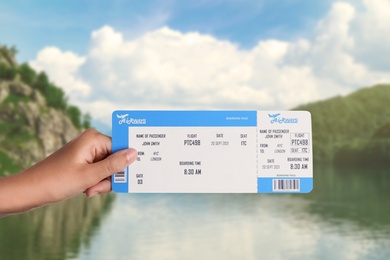 Woman holding ticket near lake and mountains, closeup. Travel agency service