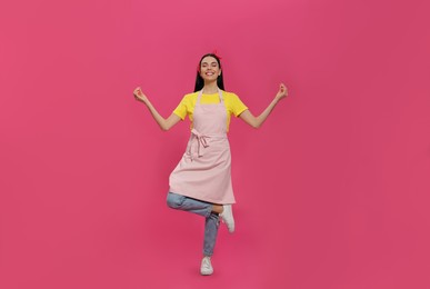 Young housewife wearing apron meditating on pink background
