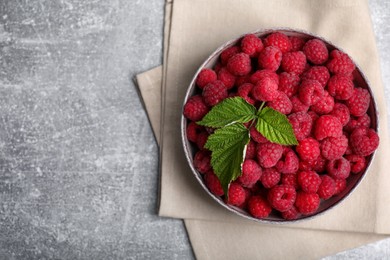 Bowl of fresh ripe raspberries with green leaves on grey table, top view. Space for text