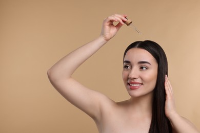 Photo of Happy young woman applying essential oil onto hair roots on beige background, space for text