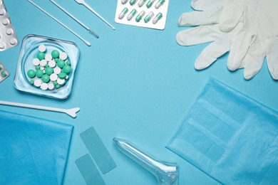 Frame of disposable gynecological examination kit and pills on light blue background, flat lay. Space for text