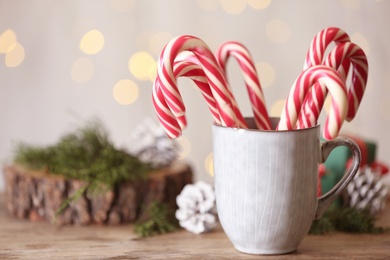 Christmas candy canes in cup on wooden table against blurred lights, space for text