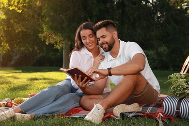 Happy young couple reading book on plaid in park. Summer picnic