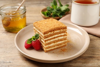 Slice of delicious layered honey cake served with mint and raspberries on wooden table