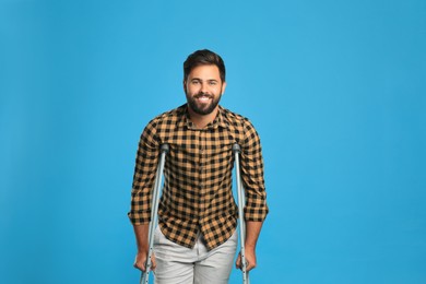 Young man with axillary crutches on light blue background